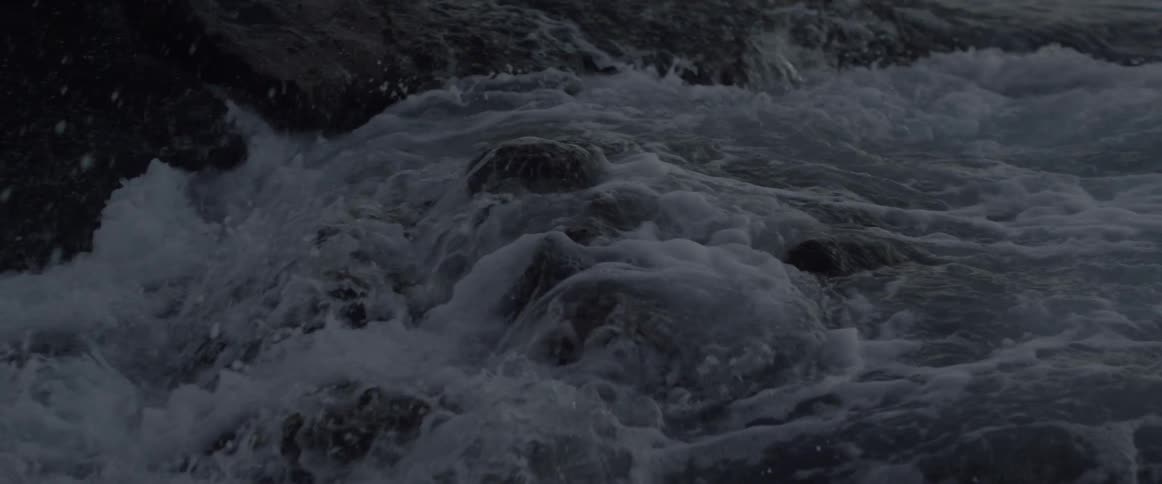 An ocean wave crashes onto a rocky shore and recedes