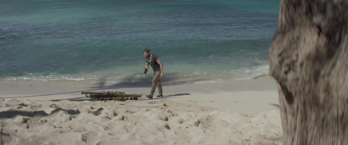 A man looks around as he walks up to a makeshift raft on a beach