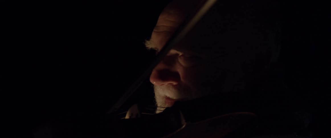 Older man plays the violin in the dark
