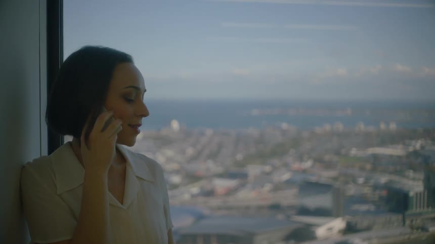 A woman talks on a cellphone as she stand in a high-rise window during the day