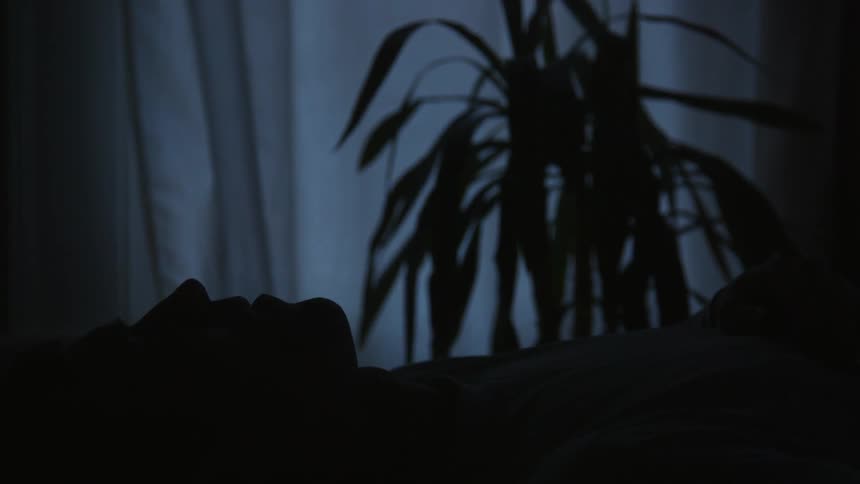 A man lies on a bed in a darkened room