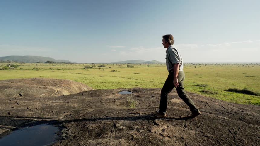 A man is walking on top of a small hill that overlooks the plains
