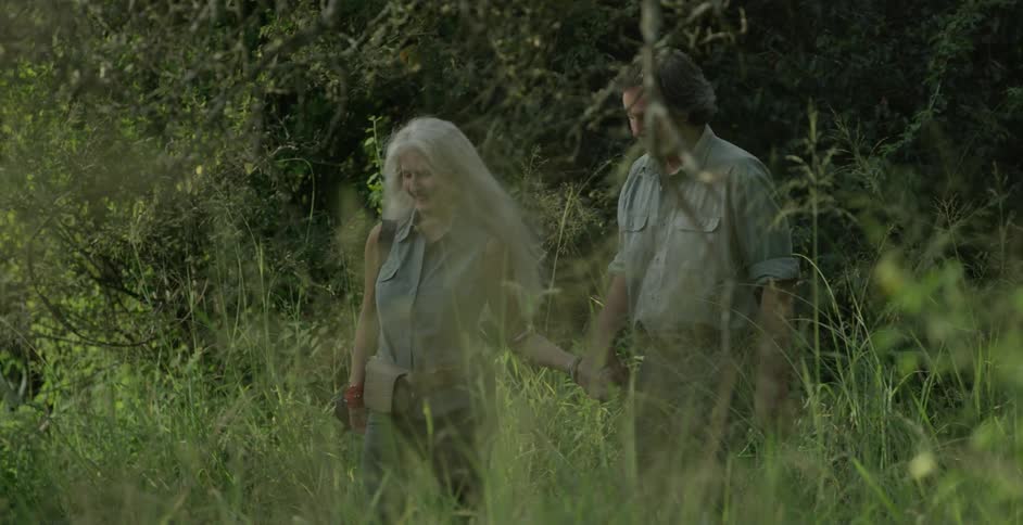 A man and woman hold hands walking through the brush