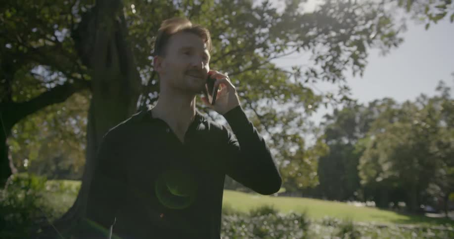 A man walking in a park during the day answers his cell phone