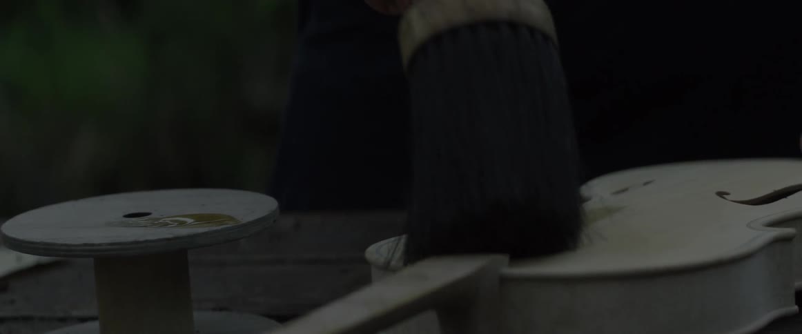 A person applies liquid to an unfinished violin with a brush