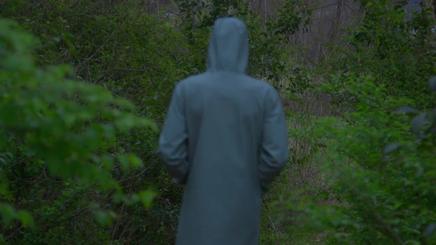 A man in a raincoat walks in a forested area