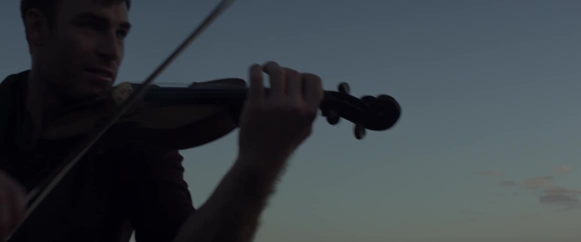 A man plays a violin outdoors at dusk
