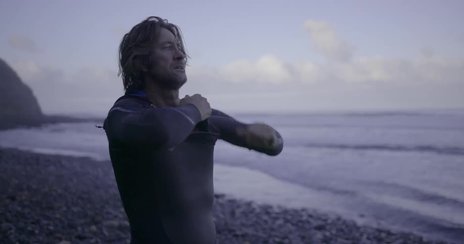 A man dons a wet suit standing on the shoreline