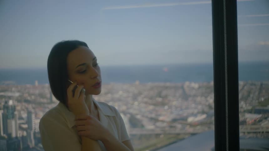 Woman talks on the phone next to a window overlooking a city