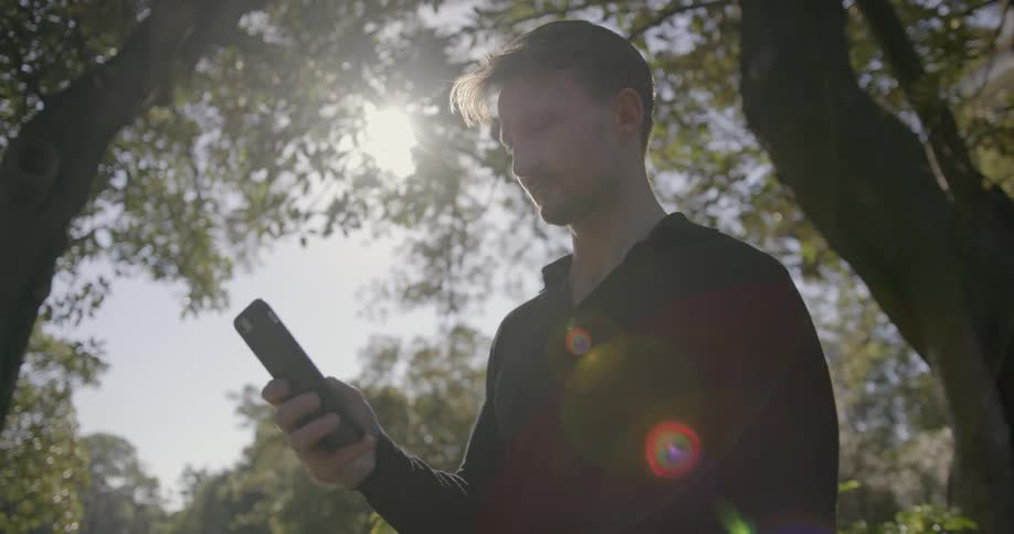 A man uses a cell phone outside under a tree