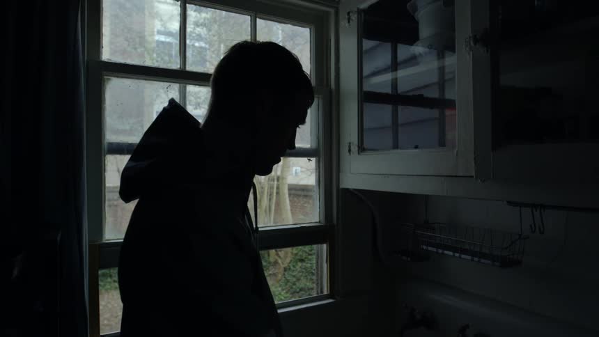 A man looks down at a sink near a window