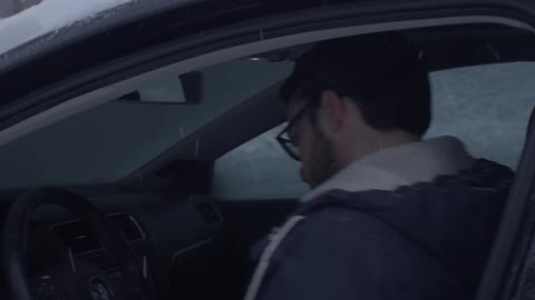 A man gets into a car covered with snow on a snowy day