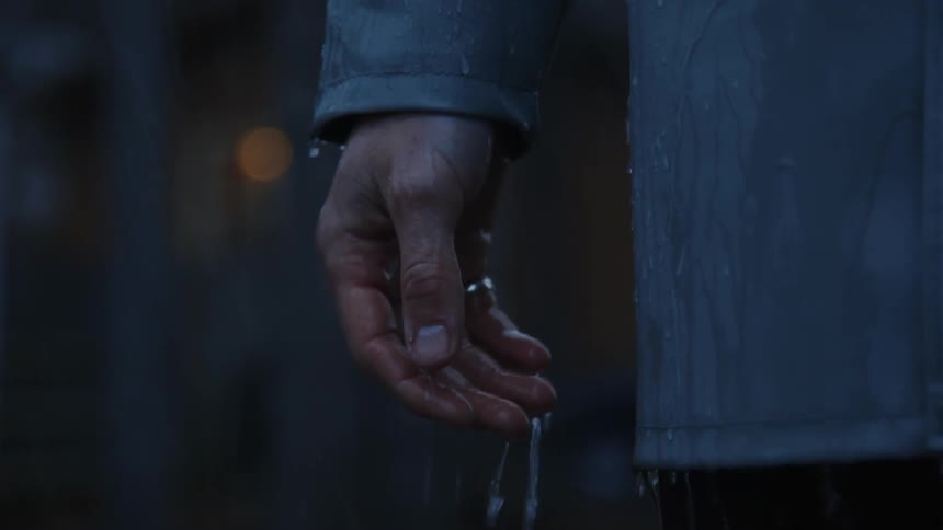 Rain drops from a man's hand and raincoat