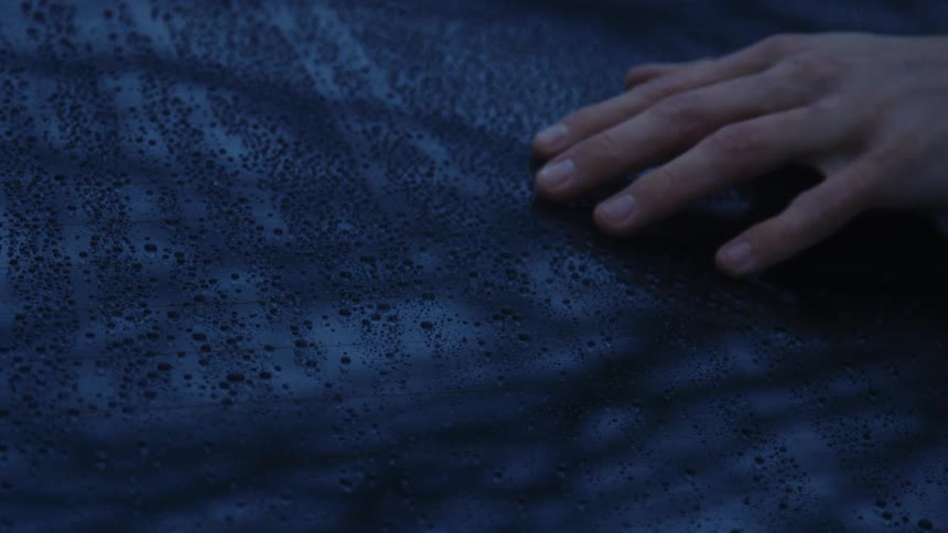 A man rubs his hand on a windshield covered with raindrops
