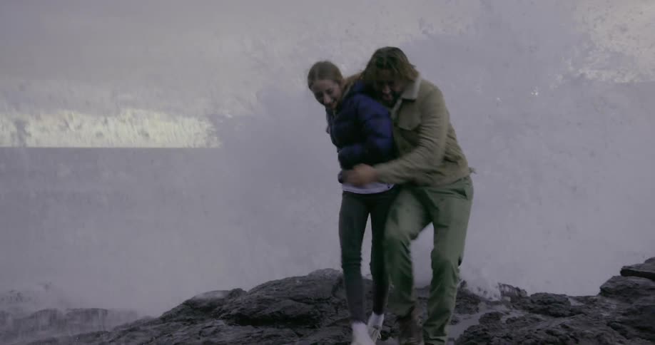 A man and woman get sprayed with water from the shore