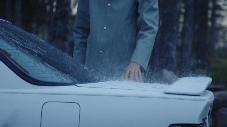 A man touches the boot of a car as water drops fall on it