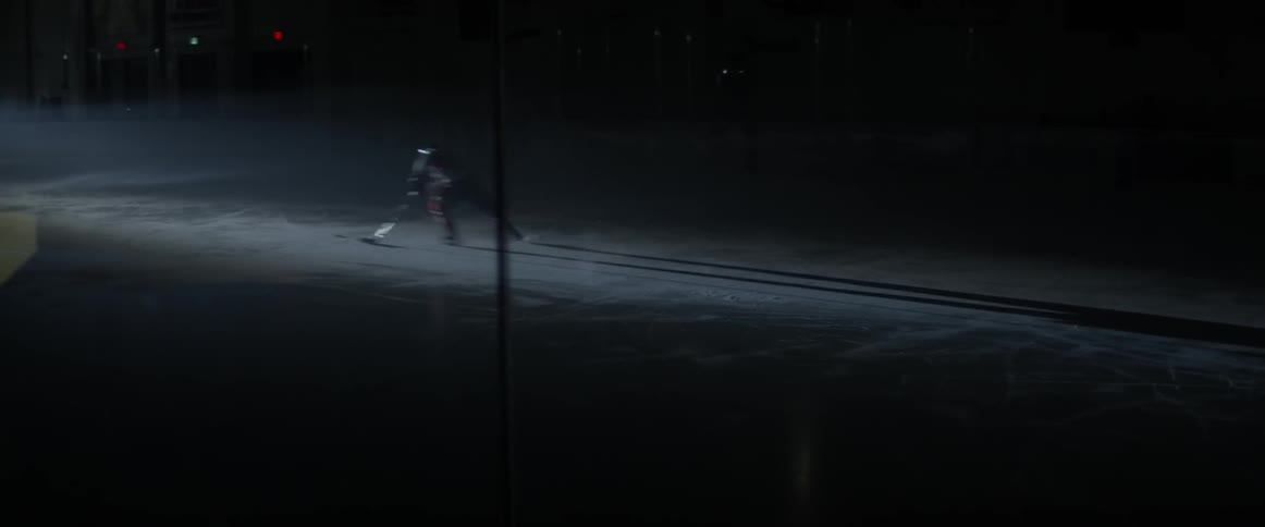 A hockey player speeds down the ice in a dark arena