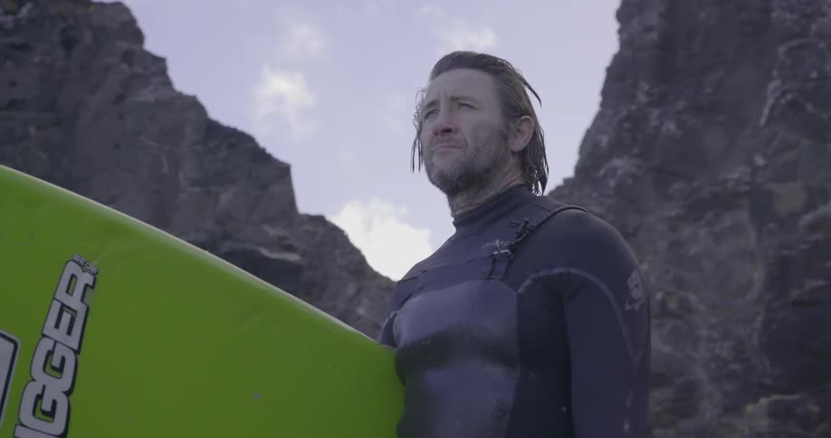 A man is standing by the rocks holding a surfboard