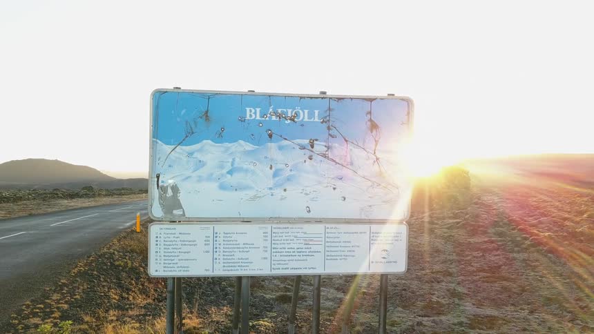 A mountain resort sign stands next to a rural road at sunset in iceland