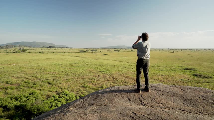 Man stands on a rock and looks into the distance using binoculars