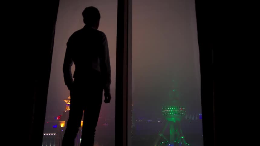 A man looks out his window overlooking a city