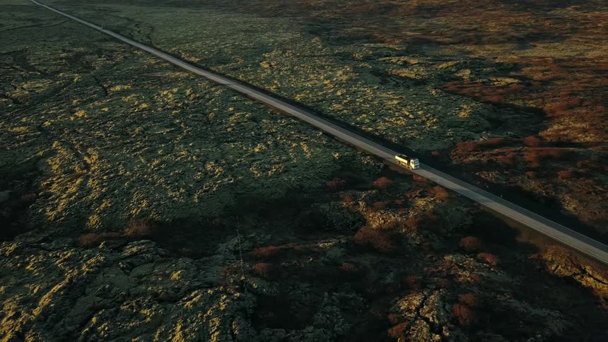 Vehicle drives down a country road surrounded by hilly plains in Iceland