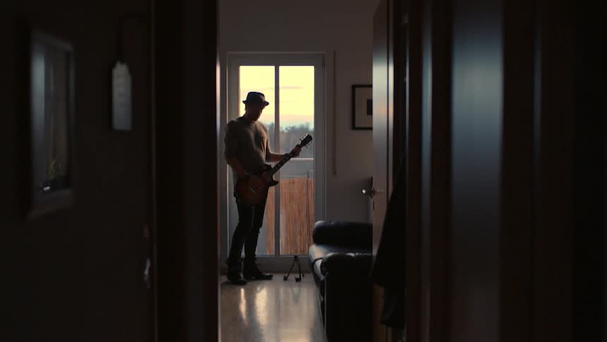 A man plays guitar next to a window