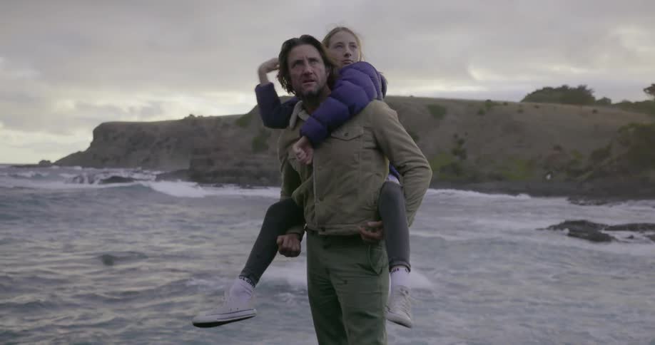 Man carries girl on his back next to water