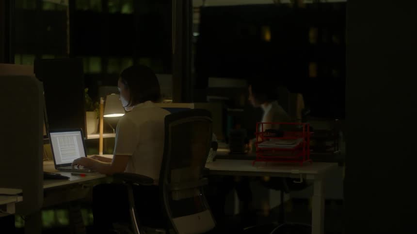 A woman types on a laptop in a dark office