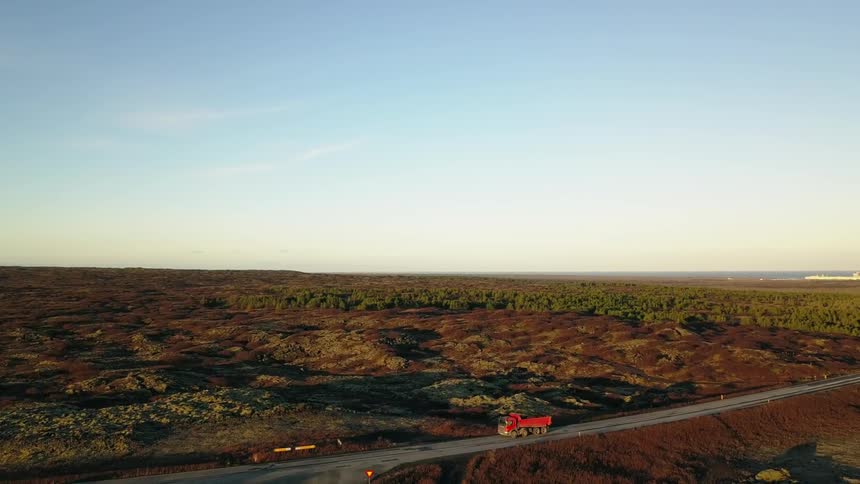 Vehicle drives down a country road surrounded by hilly lava field in Iceland