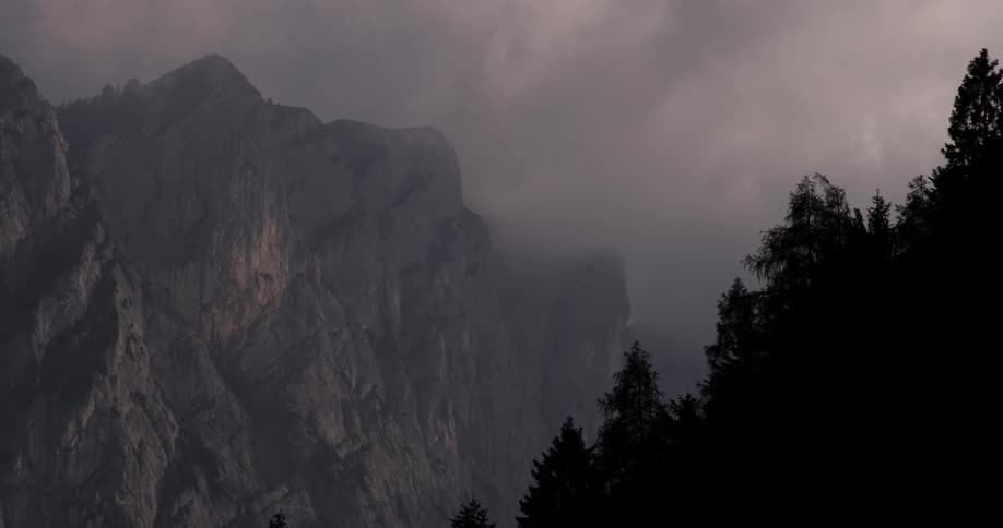 Fogs and clouds move over a mountain cliffside during the day