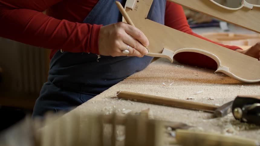 Person shaves at a piece of wood with a small metal tool