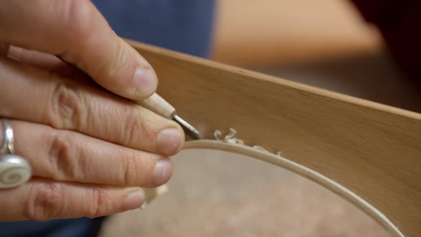 Person shaves at a piece of wood with a small metal tool