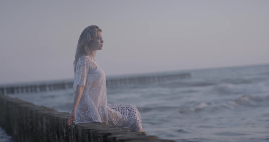 A woman in white is sitting on the edge of a pier