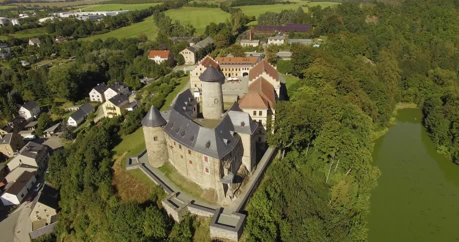 A castle like building sits atop a tree covered hillside
