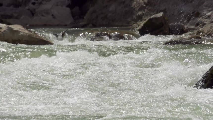 Water rushes over rocks and between boulders in a river during the day