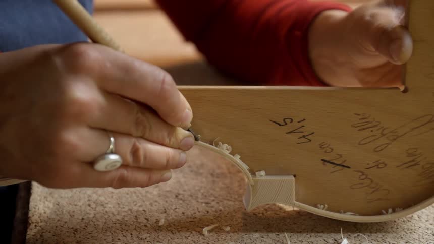 A person uses a wood carving tool to shape a piece of wood