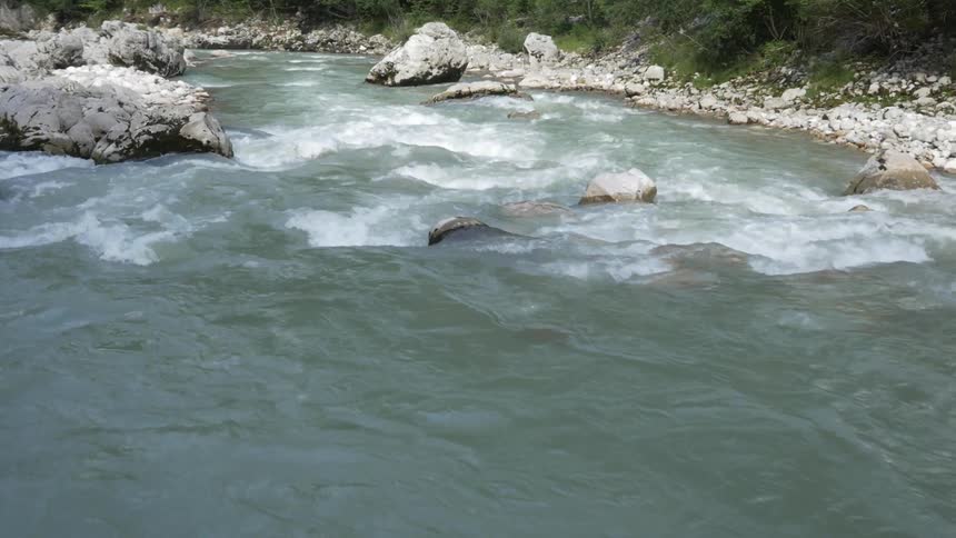 Water rushes over rocks and between boulders in a river during the day