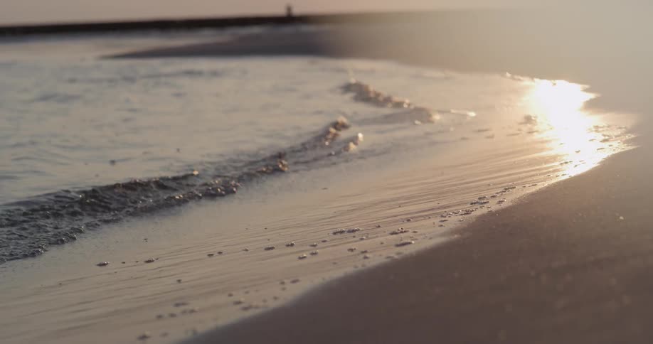 People walk on the beach as water splashes on the shore