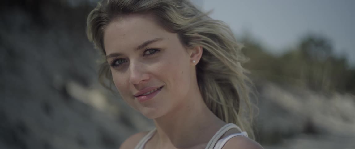 A blonde haired woman stands outside in the wind smiling