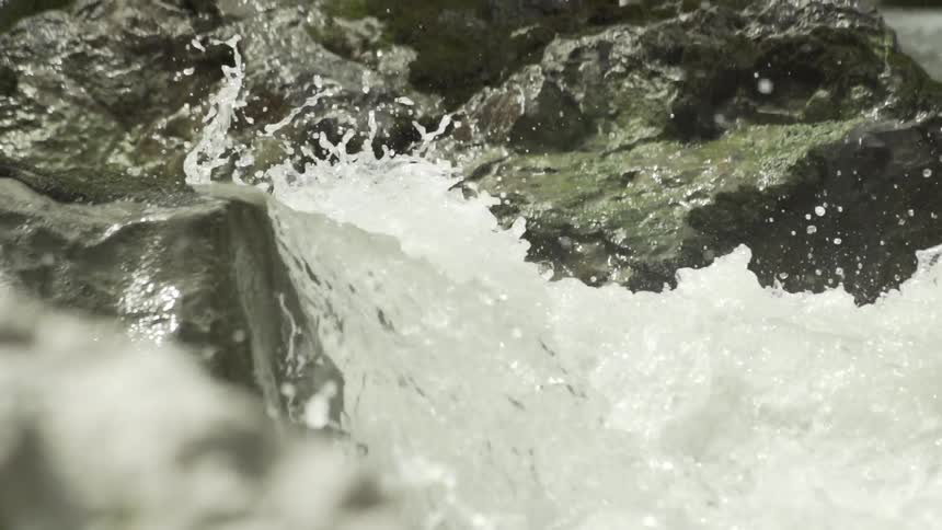 Water crashes over the rocks fast on a sunny day