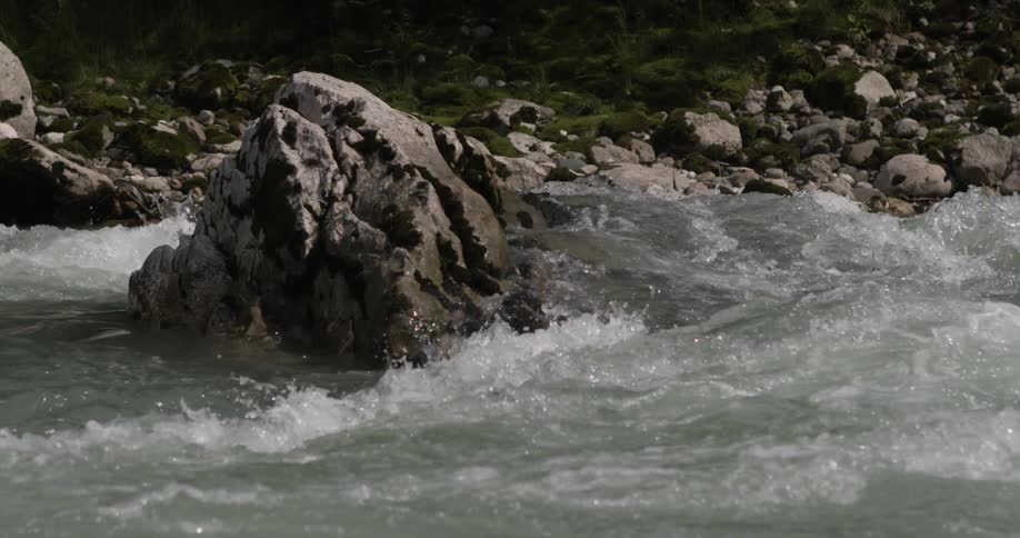 Water rushes over rocks and between boulders in a river during the day