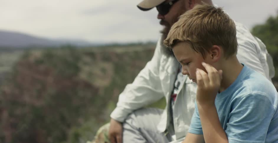 A man is pointing out something to a boy sitting next to him