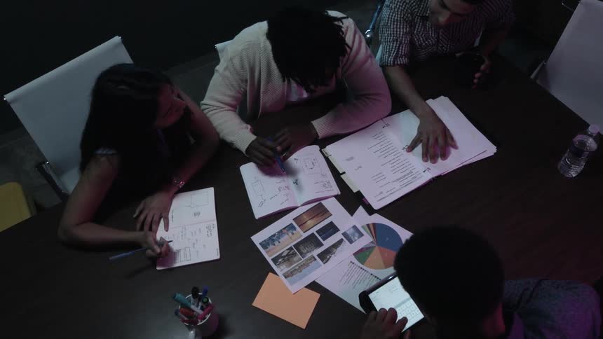 Group of people sit at a table with notebooks charts and laptop