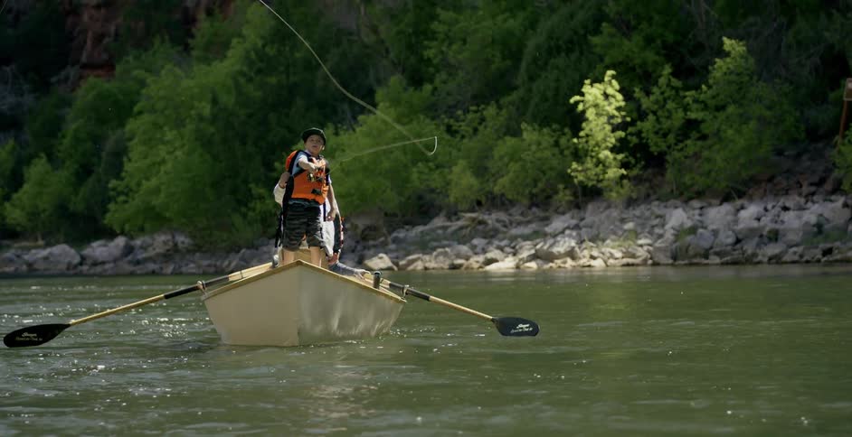 Child is fly fishing on a boat in a river