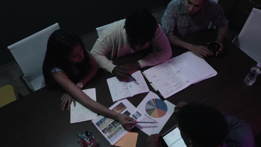 Group of people at a table looking at notebooks and charts