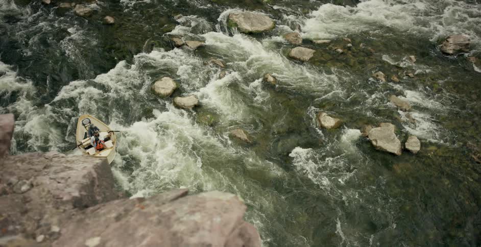 A man rows a boat over rapids in a river during the day