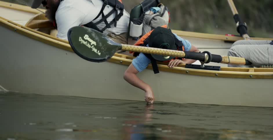 A boy moves his finger in the water of the moving boat