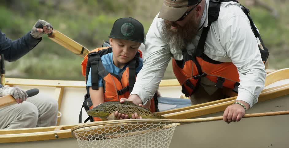 A man shows a young boy a caught fish from a net