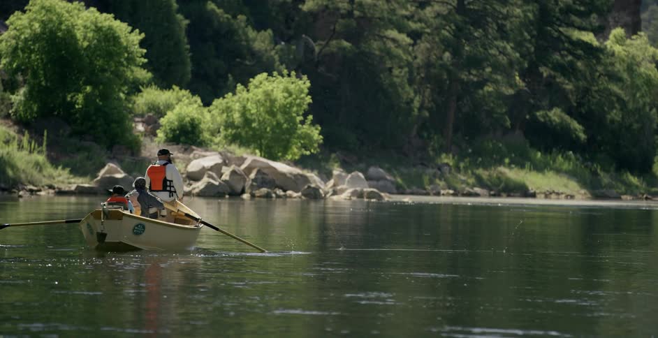 A man and boys are fishing in a row boat on a river during the day